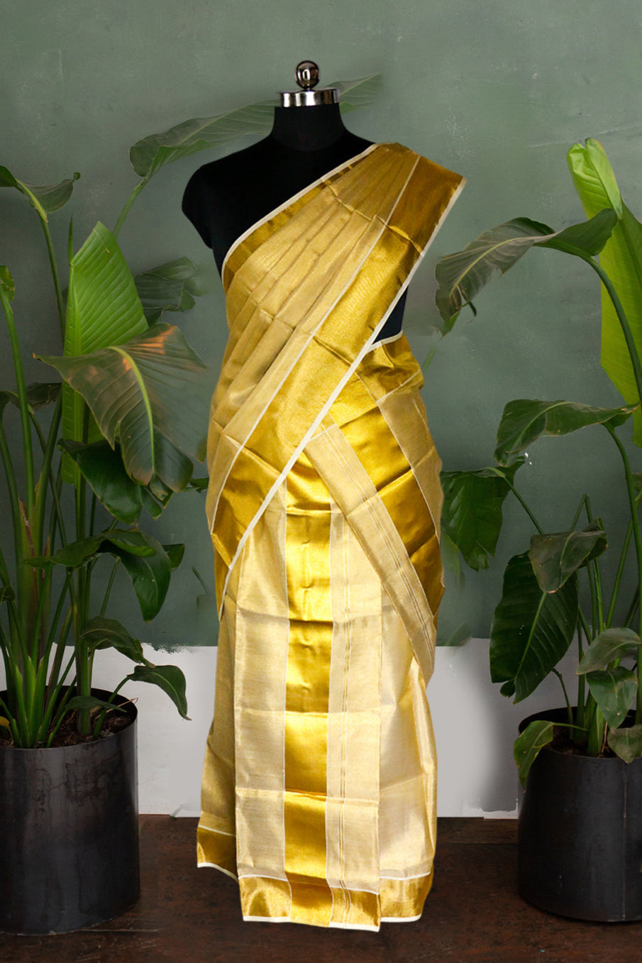 Gold saree on a mannequin with green plants in the background