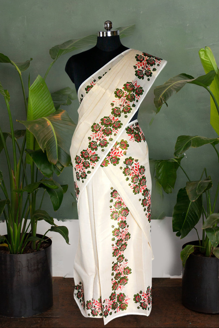 White saree with floral embroidery on a mannequin against a green wall with plants.