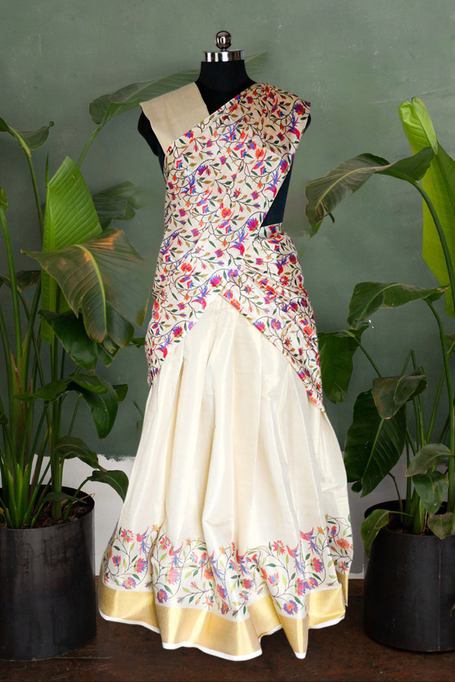 Sari with floral pattern on a mannequin against a green wall with plants.