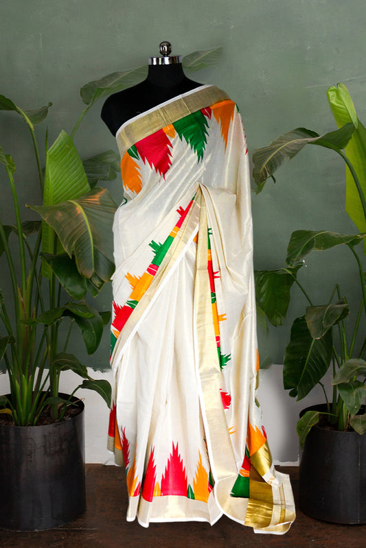 White saree with colorful patterns on a mannequin against a green wall with plants.