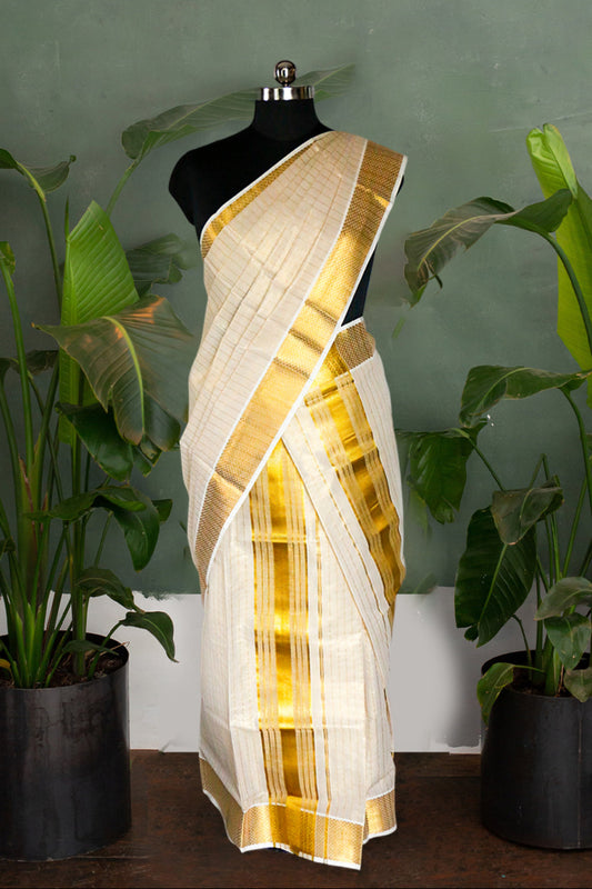 White saree with gold border on a mannequin against a green wall with plants.